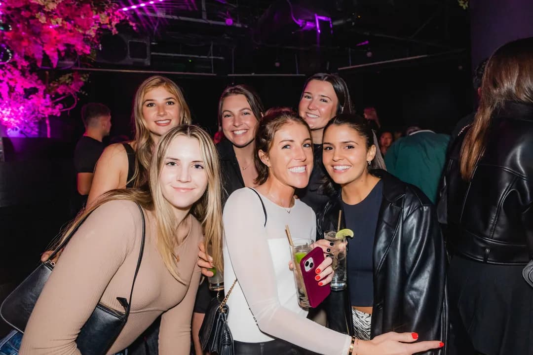 Six friends posing on the dance floor under pink party lighting