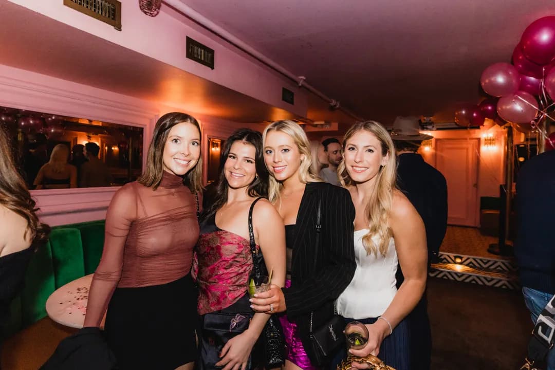 Four friends together at a birthday party beneath pink balloons